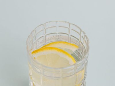 A glass of clear water with a lemon slice next to a window.